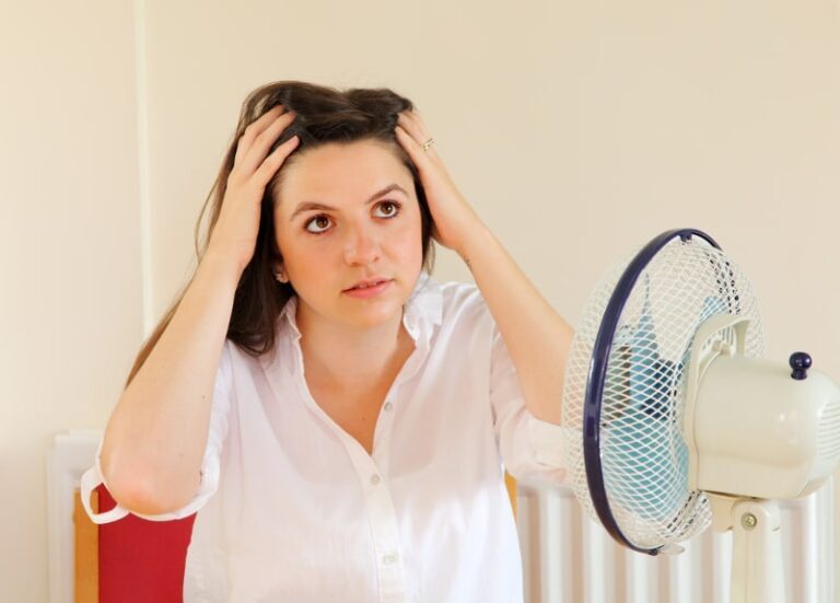 A woman clutching her head in front of a table fan.